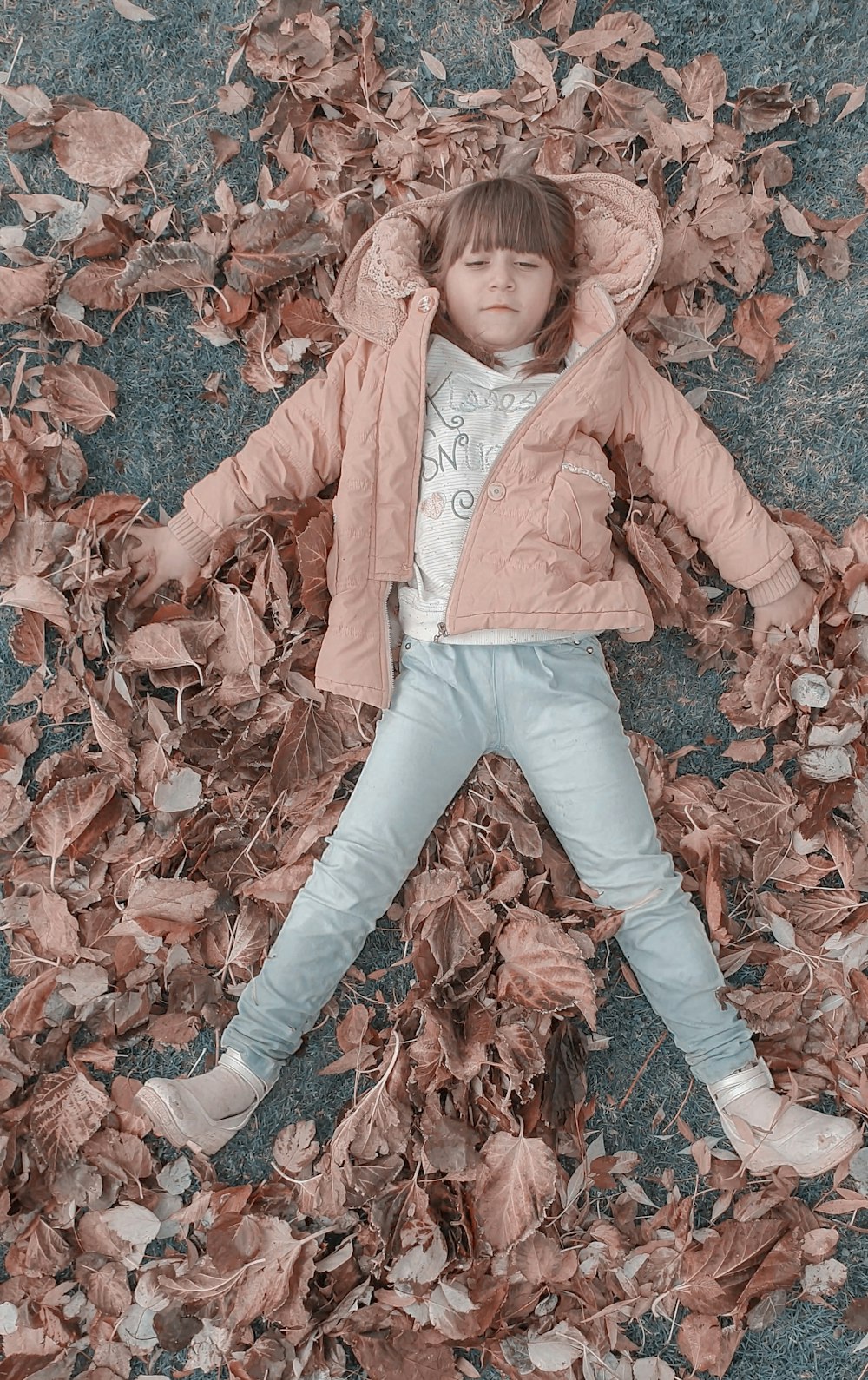 a little girl laying on top of a pile of leaves
