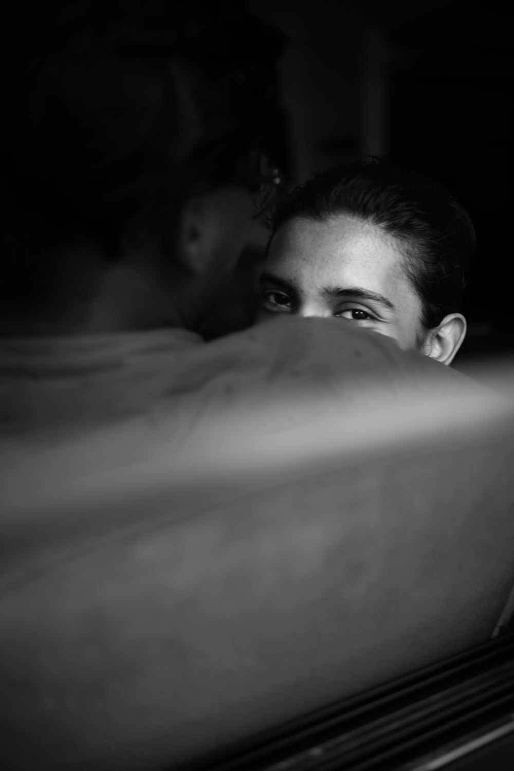 a black and white photo of a woman peeking out from behind a bed