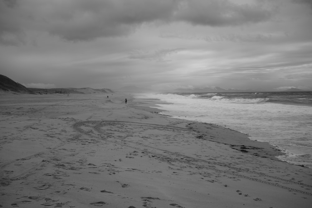 a black and white photo of a person walking on a beach