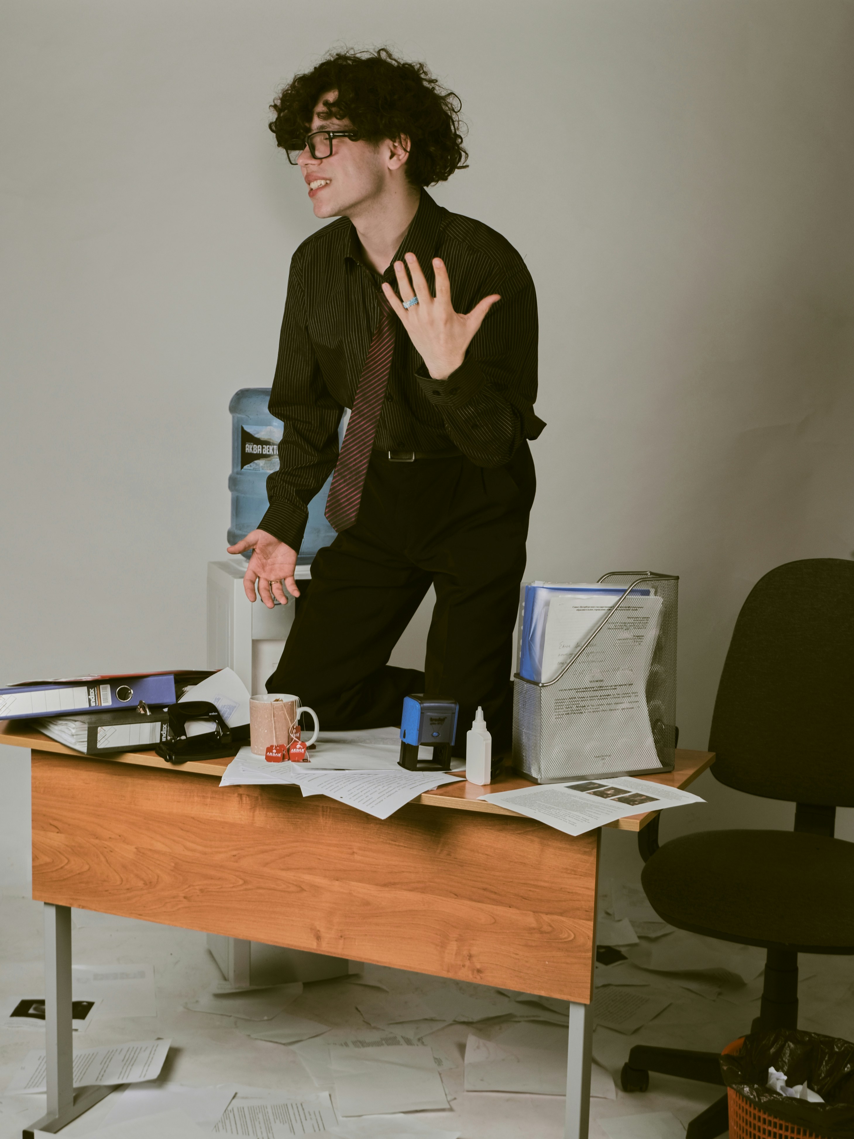 a man in a black shirt and tie standing on a desk