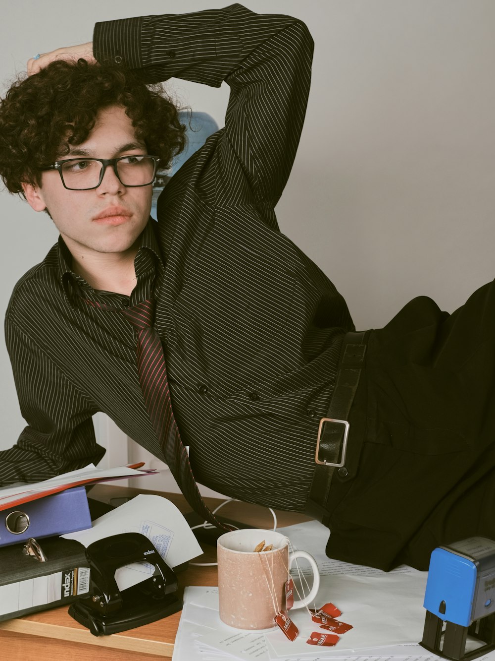 a young man with curly hair and glasses sitting at a desk