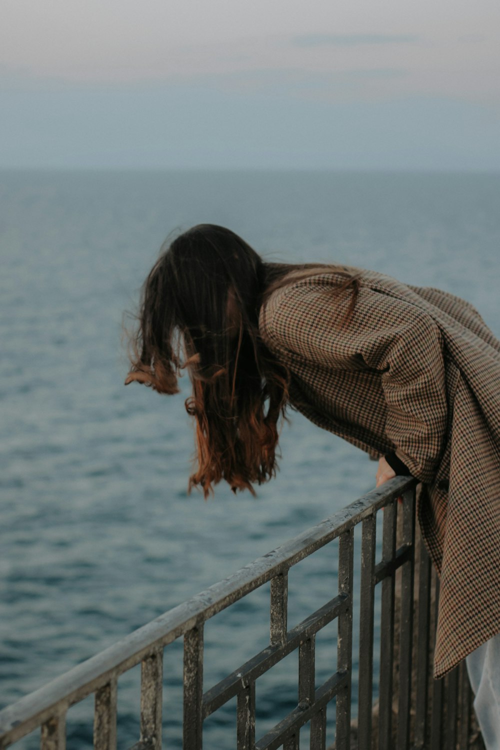 a woman leaning over a railing near the ocean