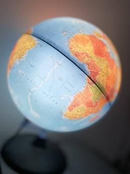 A close-up view of a globe showing parts of the Atlantic Ocean, Africa, and South America with various countries marked in different colors. The globe is mounted on a stand and has a soft light illuminating it, suggesting a warm and inviting atmosphere.