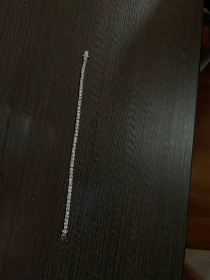 A delicate bracelet made from fine steel resting gently on a linen cloth with green leaves nearby.