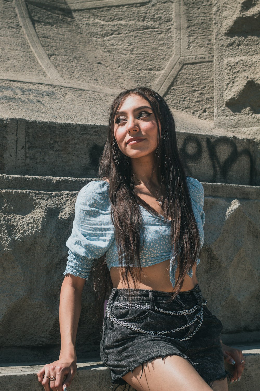 a woman sitting on a stone wall with her legs crossed