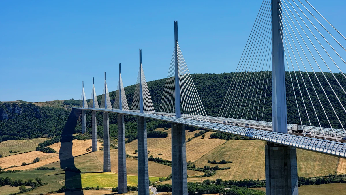 The Millau Viaduct crossing farmland and wooded hills under a blue sky