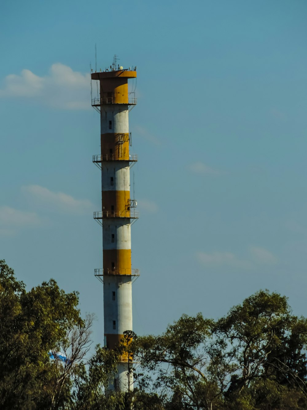 a tall white and yellow tower with trees in the background