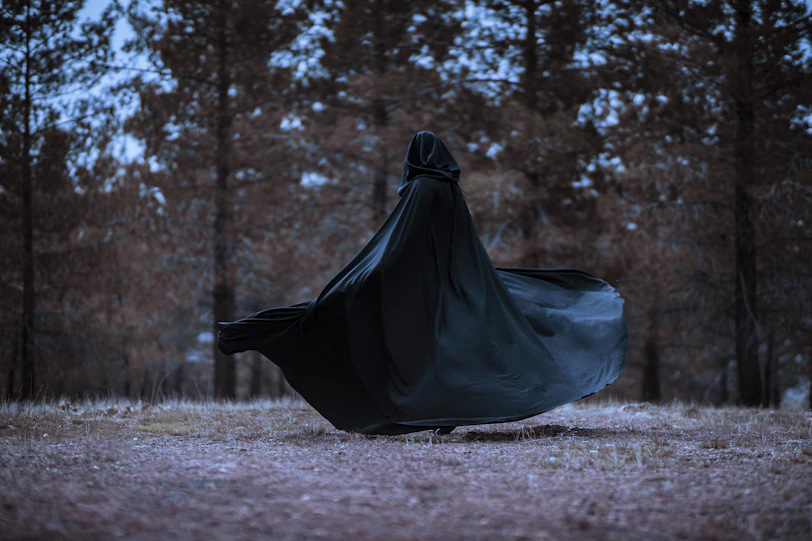 a woman in a black cloak is walking through the woods