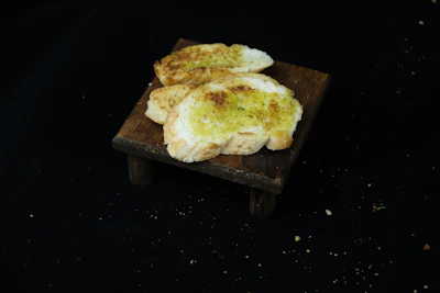 Warm, golden-brown garlic bread slices arranged neatly on a white plate with a side of dipping sauce.