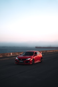 A shiny red convertible parked on a coastal road with ocean views.