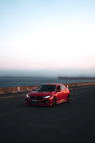 A sporty red convertible cruising along a coastal highway with ocean waves in the background.