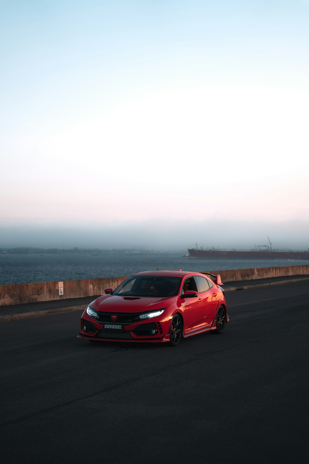 a red car driving down a road next to the ocean