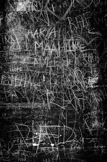Chaotic scribbles and faded words layered over a dimly lit room, hinting at the fragmented thoughts within.