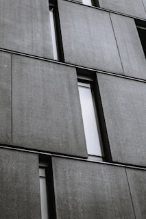 Several large, rectangular concrete panels are arranged in a grid pattern on the facade of a modern building. The panels have a textured surface and are separated by narrow, vertical window slits.