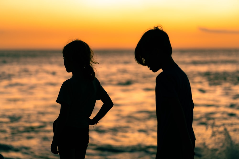 a couple of kids standing next to each other near the ocean