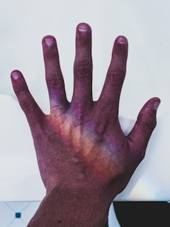 A human hand with the palm facing down, illuminated by a spectrum of colors resembling a rainbow effect. The background is a plain white surface.
