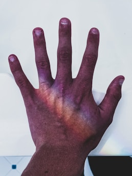 A human hand with the palm facing down, illuminated by a spectrum of colors resembling a rainbow effect. The background is a plain white surface.