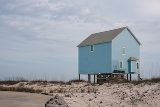 A serene blue house with a 'For Sale' sign in front.