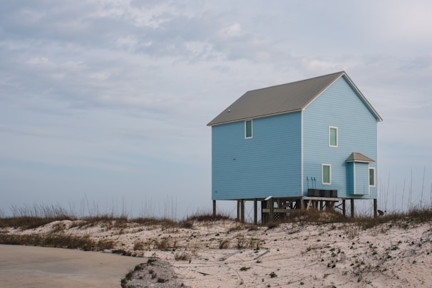 A serene blue house with a 'For Sale' sign in front.