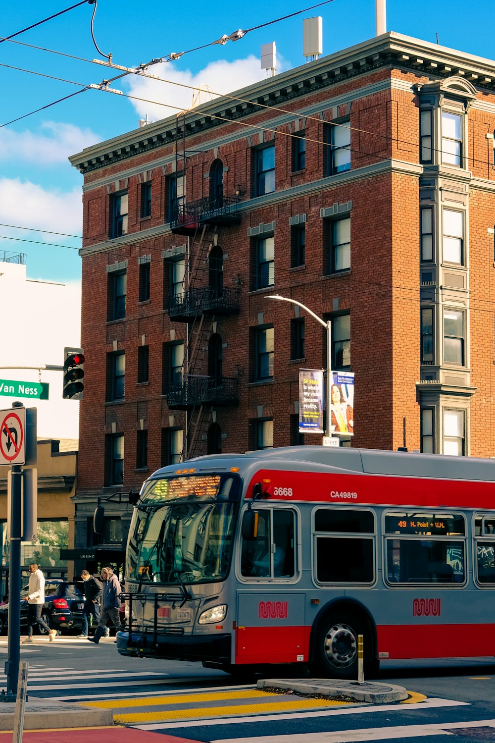 a red and gray bus driving down a street next to a tall building