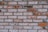 A detailed view of a brick wall with a mix of reddish-brown and gray bricks. The surface shows signs of aging and wear, with some bricks displaying patches of white residue or paint. The layout is in a traditional horizontal pattern with visible mortar lines between the bricks.