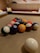 A set of billiard balls arranged on a pool table. The balls are colorful, featuring numbers, and the surrounding environment includes wooden panel walls and cushioned seating.