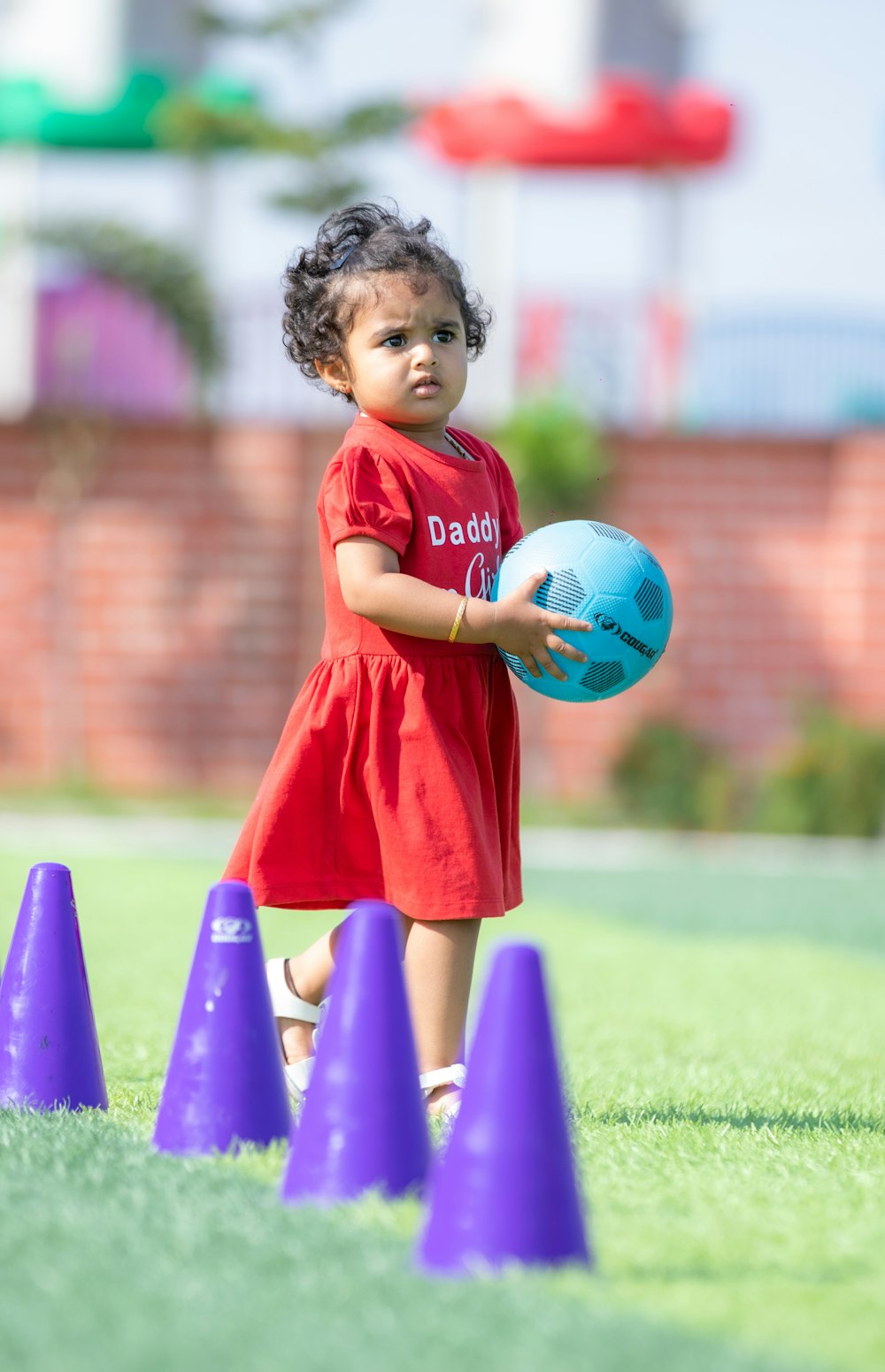 a little girl in a red dress holding a blue ball