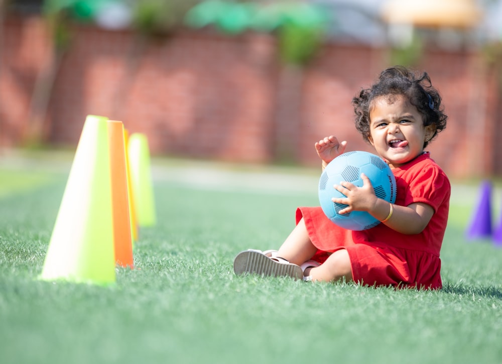 a small child sitting on the ground with a ball