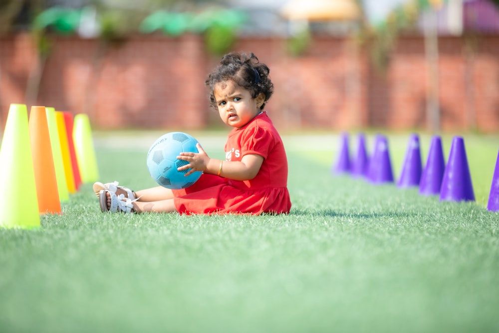 a small child sitting in the grass with a ball