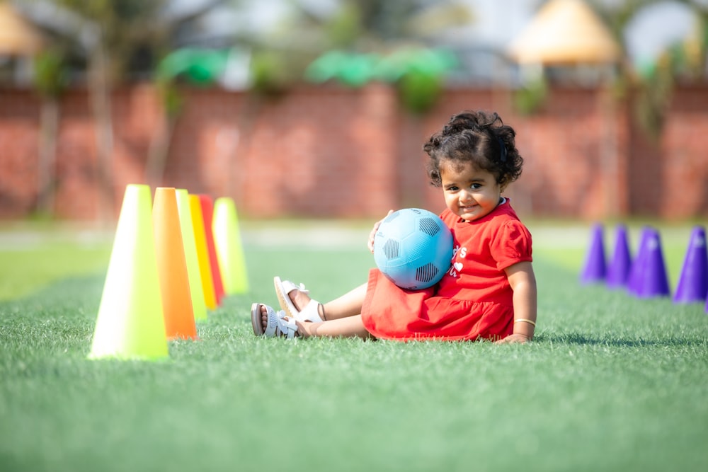 a little girl sitting in the grass with a ball