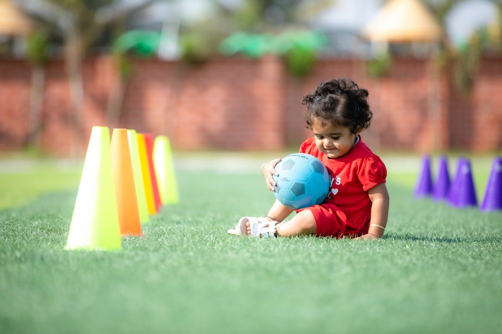 a small child sitting on the ground with a ball