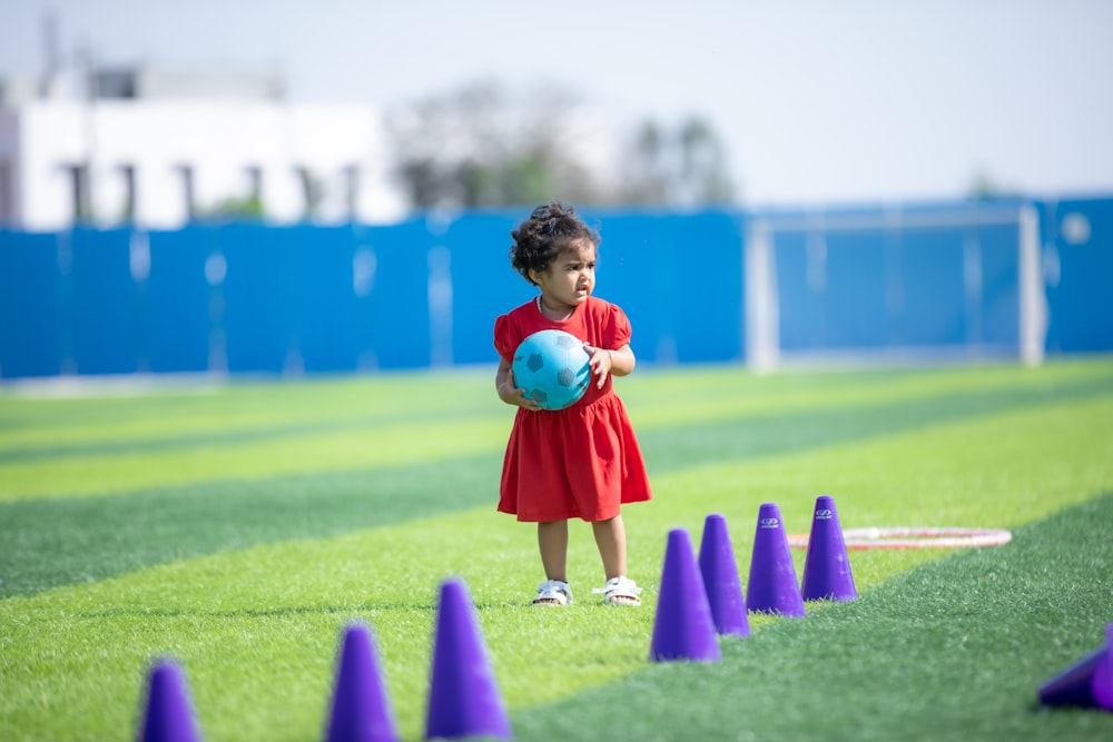 a little girl in a red dress holding a soccer ball