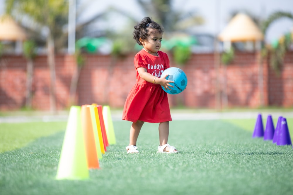 a little girl in a red dress holding a blue ball