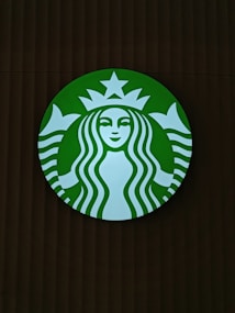 A round green logo with a white silhouette of a twin-tailed siren in the center. The siren has long wavy hair, a serene facial expression, and is framed by a circular band with a star above her head.