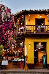 a yellow building with a balcony and tables outside