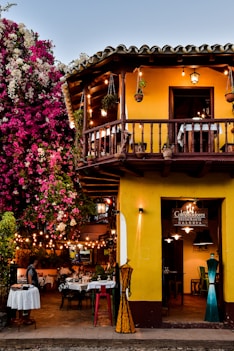 a yellow building with a balcony and tables outside