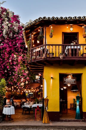 a yellow building with a balcony and tables outside