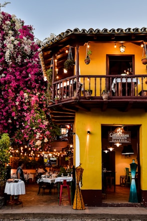 a yellow building with a balcony and tables outside