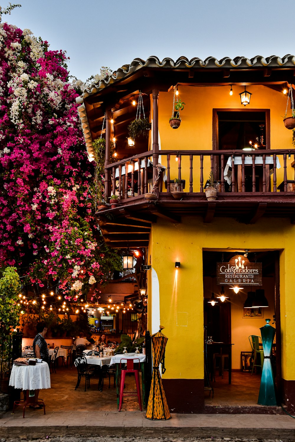 a yellow building with a balcony and tables outside