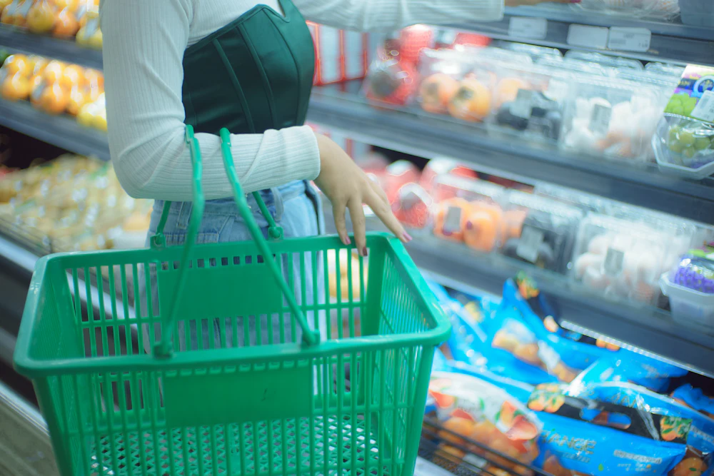 A shopper with a basket choosing between products in a chilled aisle.