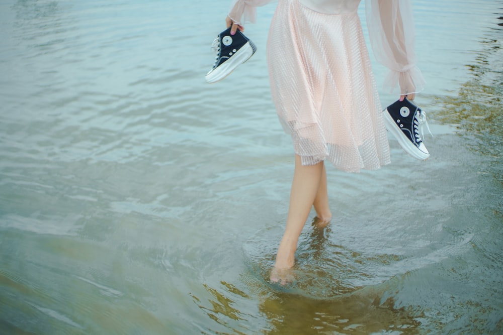 a woman walking in the water with a pair of sneakers