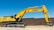 A large yellow excavator with the brand name visible on its arm is parked on a construction site. The machine has a long arm and is resting on a dirt ground in front of a brown brick wall under a clear blue sky.
