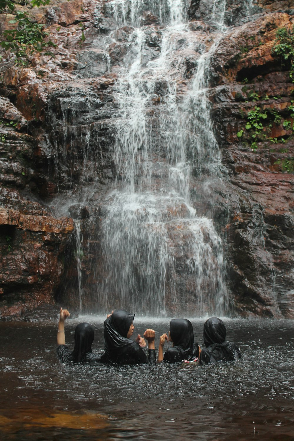 a group of people sitting in the water near a waterfall