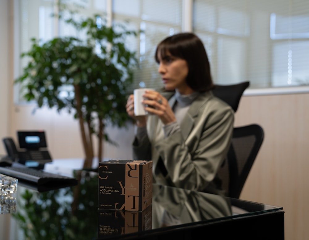 a woman sitting at a desk holding a cup of coffee