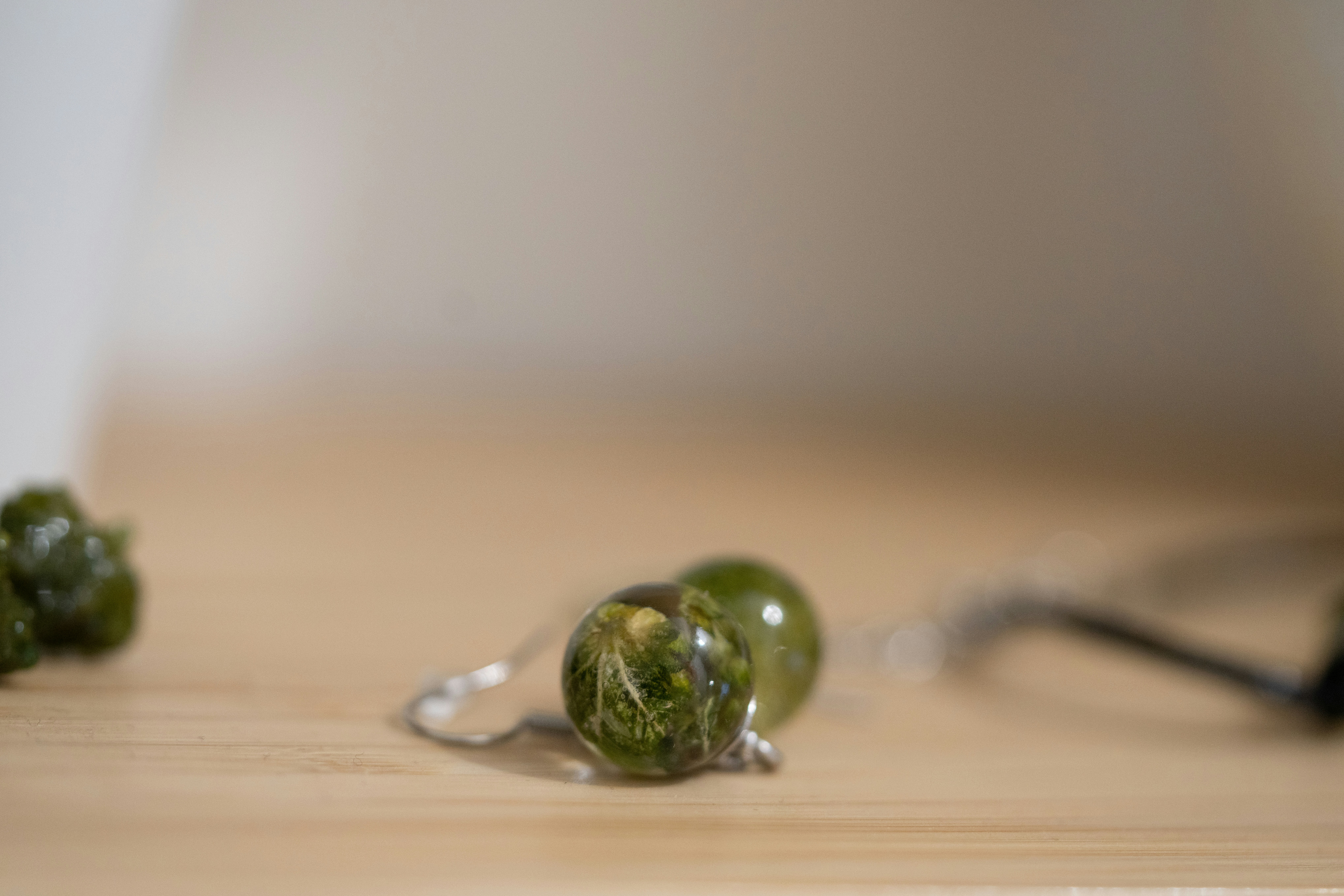 Pair of translucent blue-green resin teardrop earrings hanging on a natural wood display, warm soft lighting