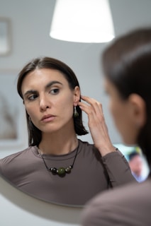 A woman adjusting her necklace in front of a mirror.