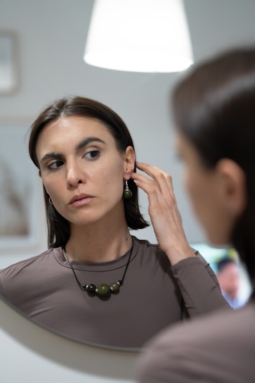 Close-up of a woman adjusting her earrings, her reflection showing quiet confidence before heading out.