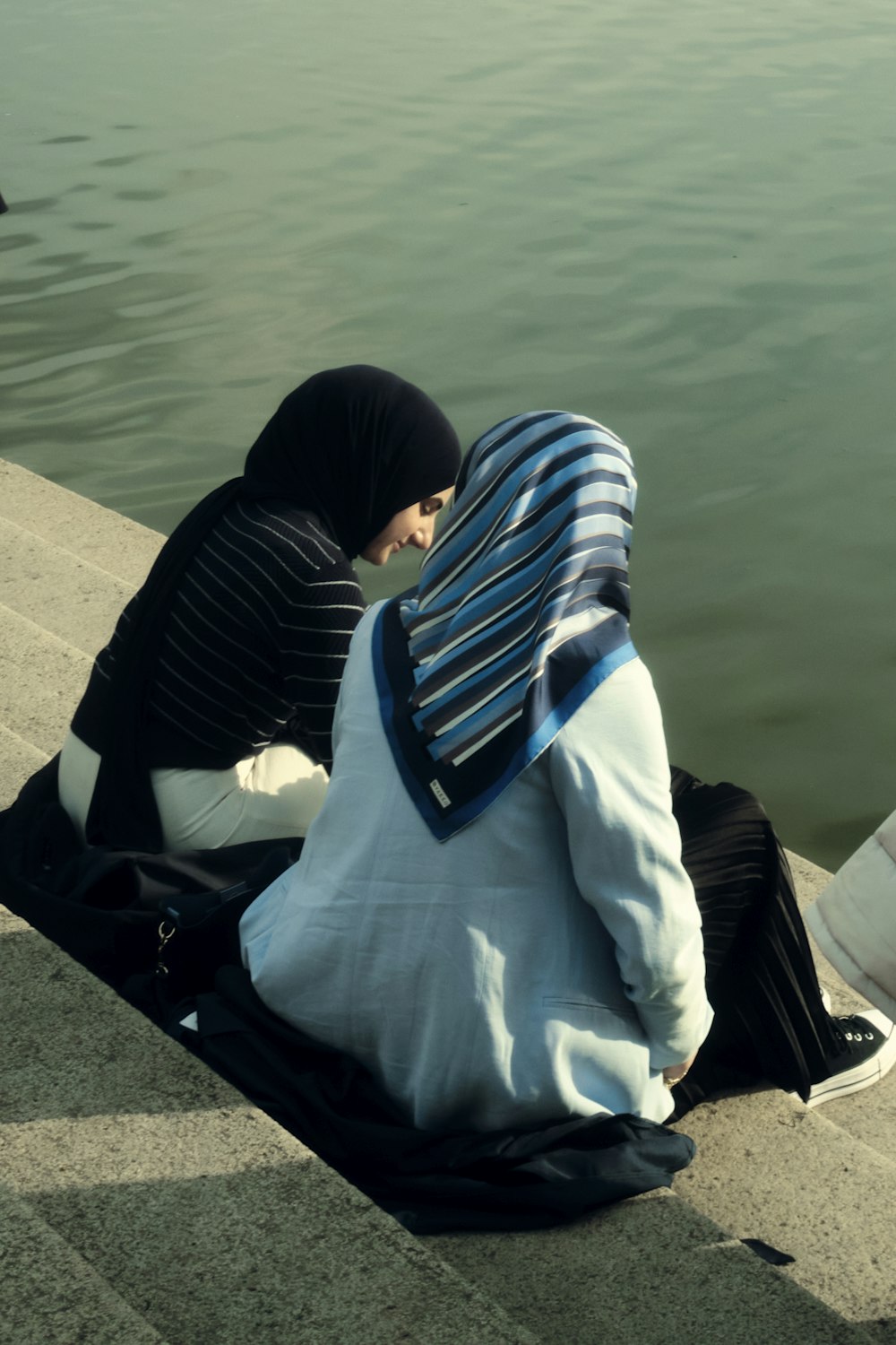 a couple of people sitting next to a body of water