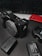 A digital camera, likely a Sony model, is placed on a dark surface. Accompanying items include camera batteries, a battery charger, and a red smartphone. A keyboard is visible in the background, suggesting a workspace environment.