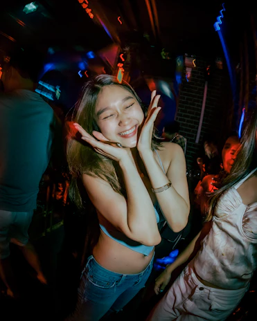 Close-up of smiling girls dancing with hands in the air, surrounded by glowing party lights.